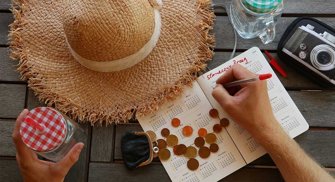 a hand writing on a book with coins and a straw hat