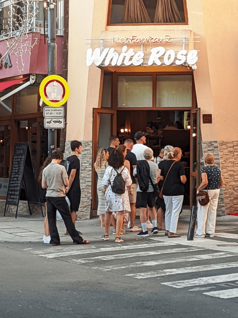 Kolejka turystów przed restauracją Biała Róża w Nesebarze — goście czekają w słońcu na wolny stolik